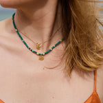 Close-up of a person wearing a green beaded necklace with gold pendants on a blurred natural background.