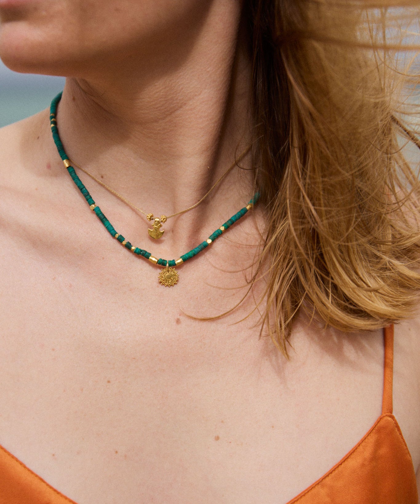 Close-up of a person wearing a green beaded necklace with gold pendants on a blurred natural background.