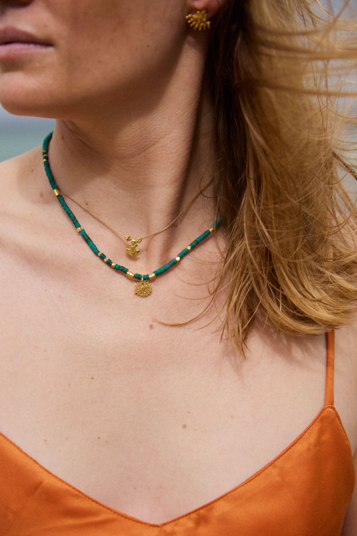 Close-up of a person wearing a green beaded necklace with gold pendants on a blurred natural background.